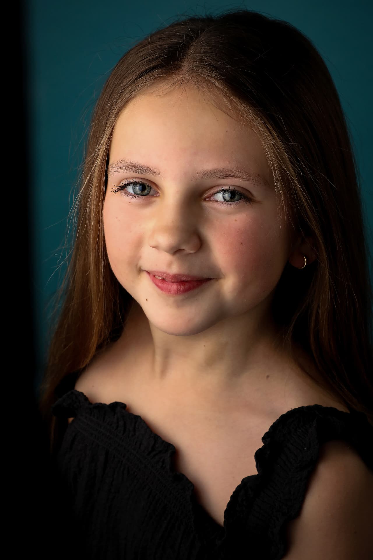 Close-up portrait of Olivia in a black ruffle top against a teal backdrop