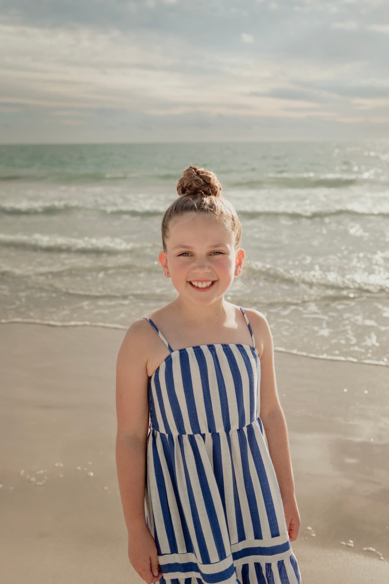 Olivia smiling on the beach in a blue and white striped dress