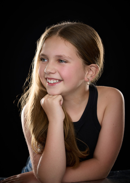 Olivia smiling warmly with her chin on her hand in a studio portrait on a black backdrop