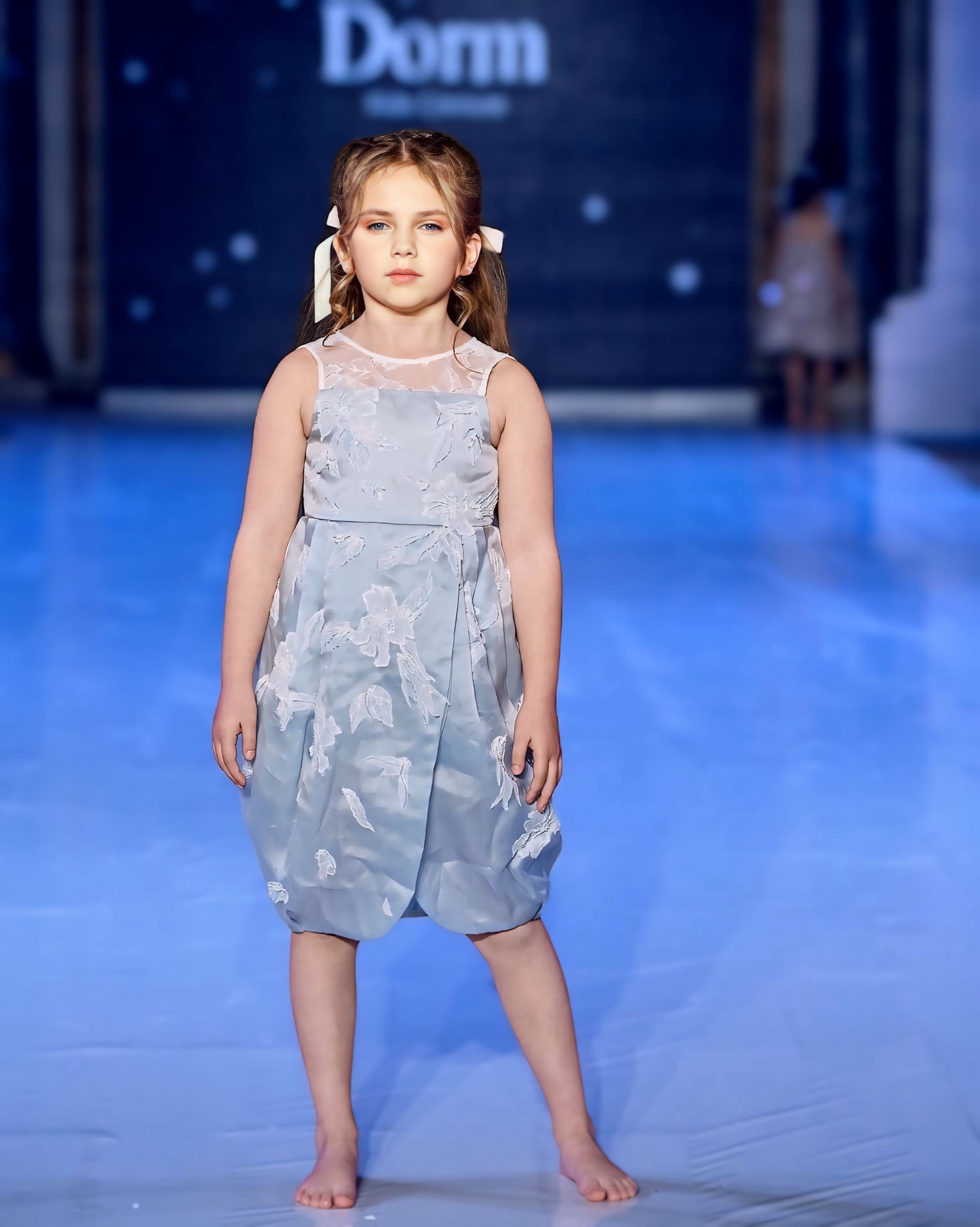 Olivia on the runway in a light blue floral dress for Dorm Kids Couture