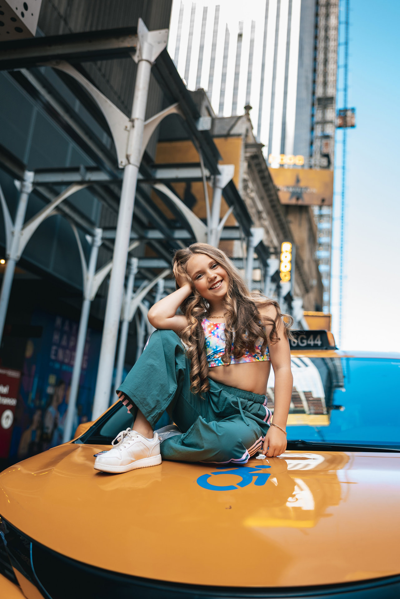 Olivia smiling while seated on the hood of a yellow NYC taxi near Broadway theatres
