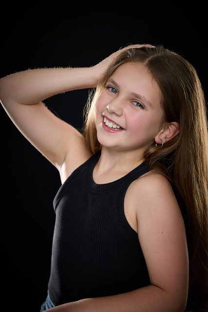 Olivia laughing with one hand behind her head in a studio portrait on a black backdrop