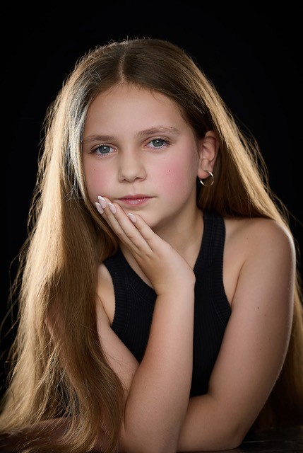 Olivia resting her chin on her hand in a serene studio portrait on a black backdrop