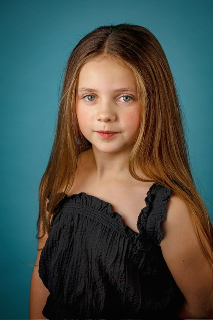 Studio headshot of Olivia against a teal backdrop, wearing a black top
