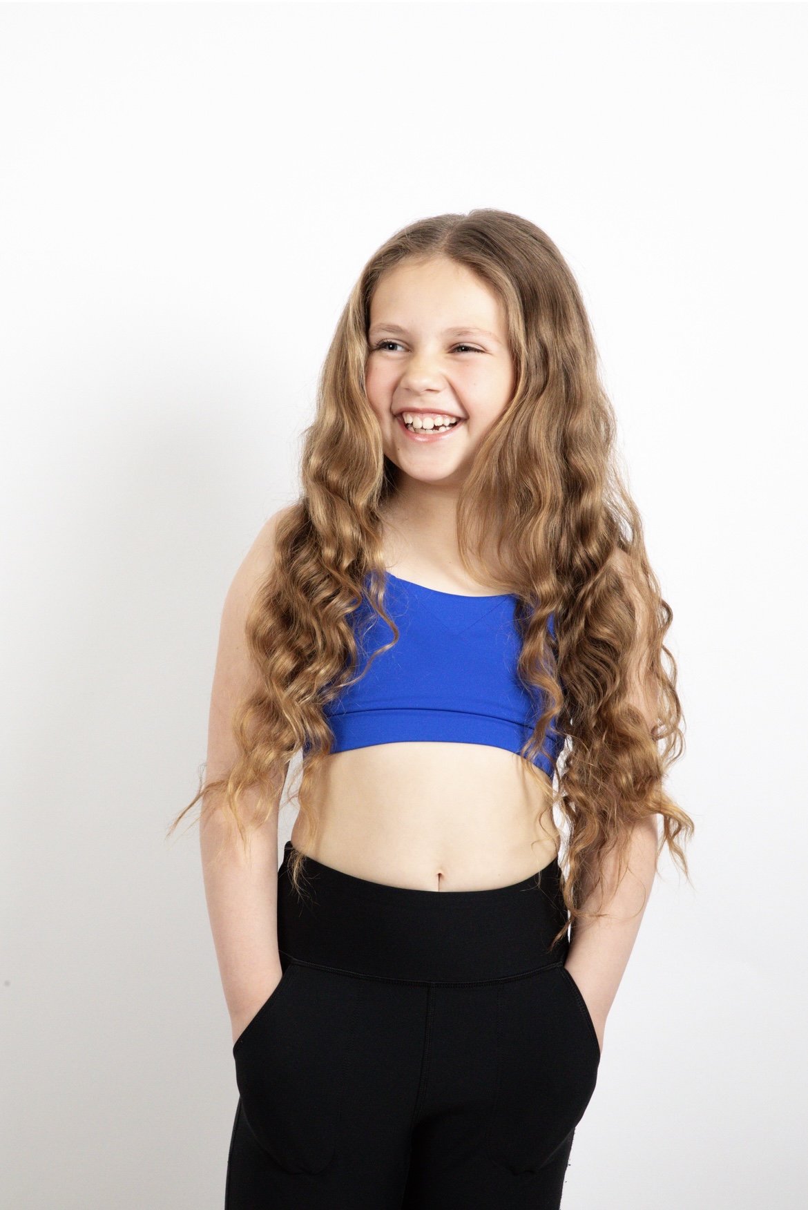 Olivia laughing in a royal blue top and black leggings against a white studio backdrop
