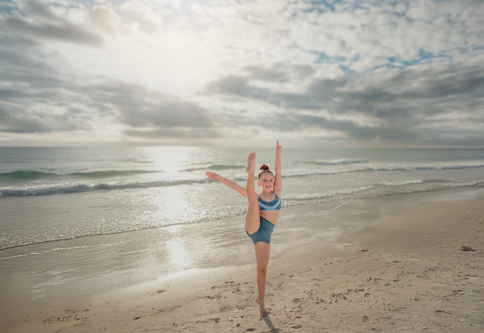 Olivia holding a high leg extension on the shoreline under a bright sky