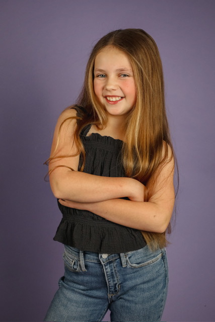 Olivia smiling with arms crossed against a purple studio backdrop