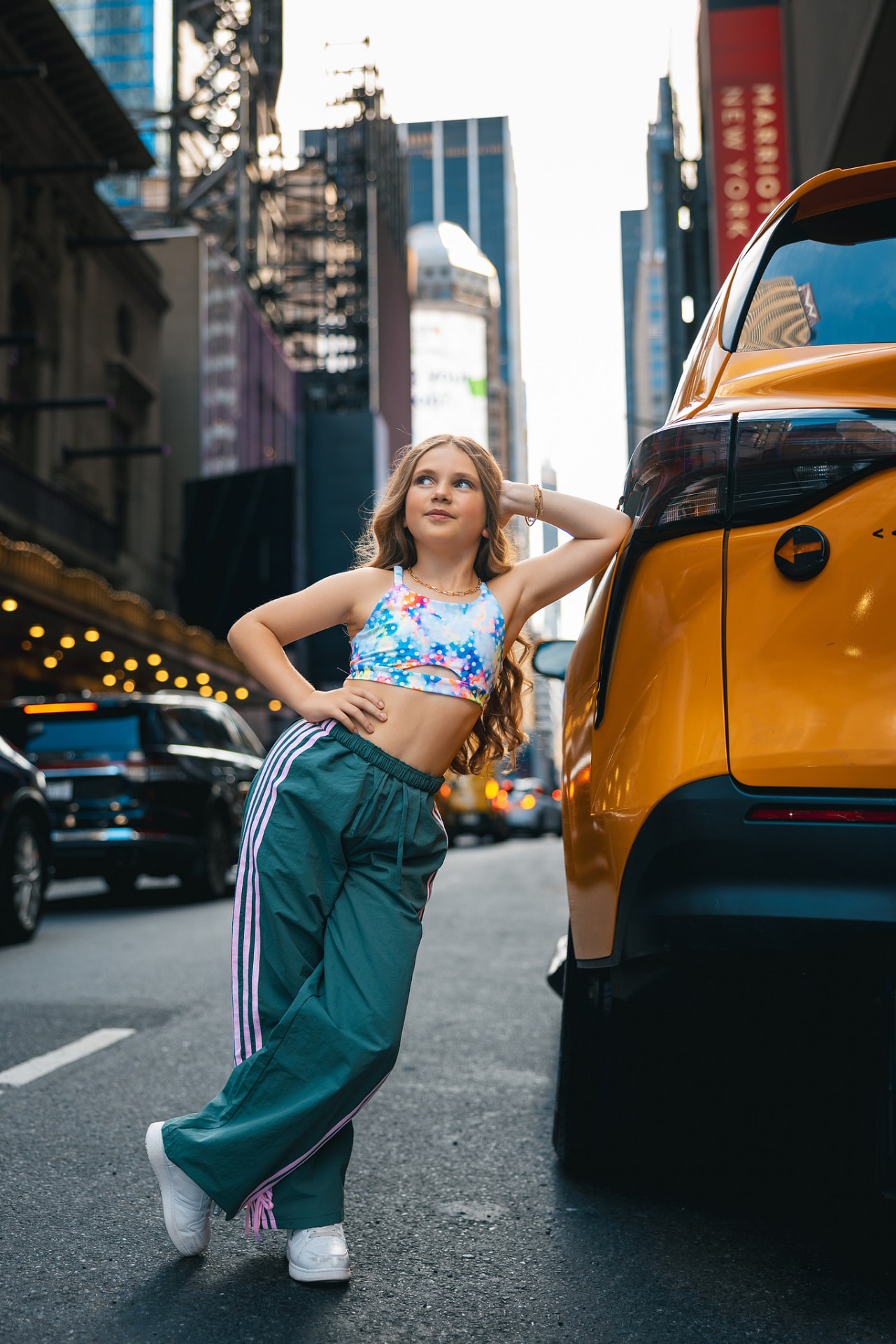 Olivia posing against a yellow taxi in Times Square in a colourful crop top and green track pants