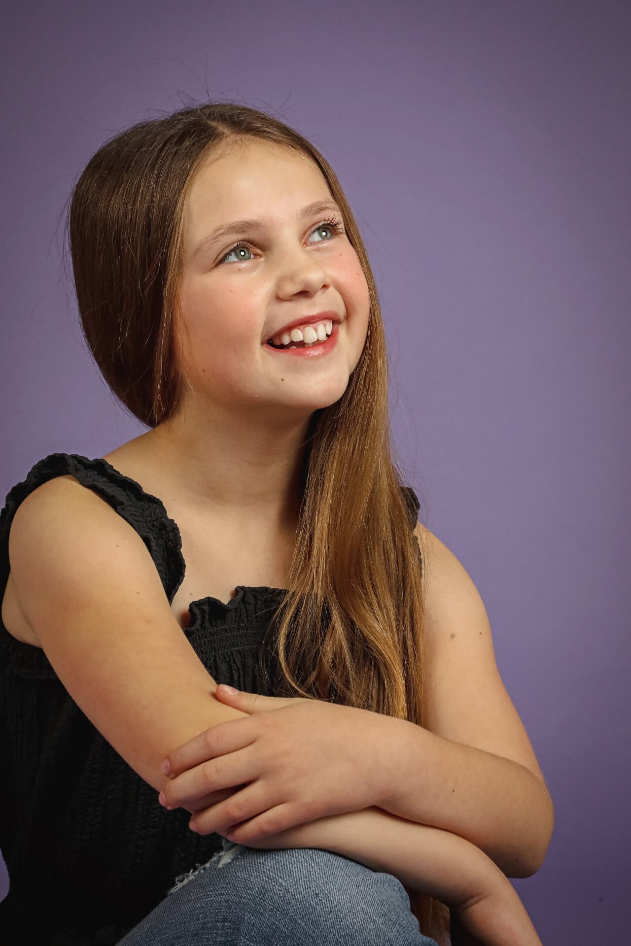 Olivia seated against a purple backdrop in a black ruffle top, gazing upward