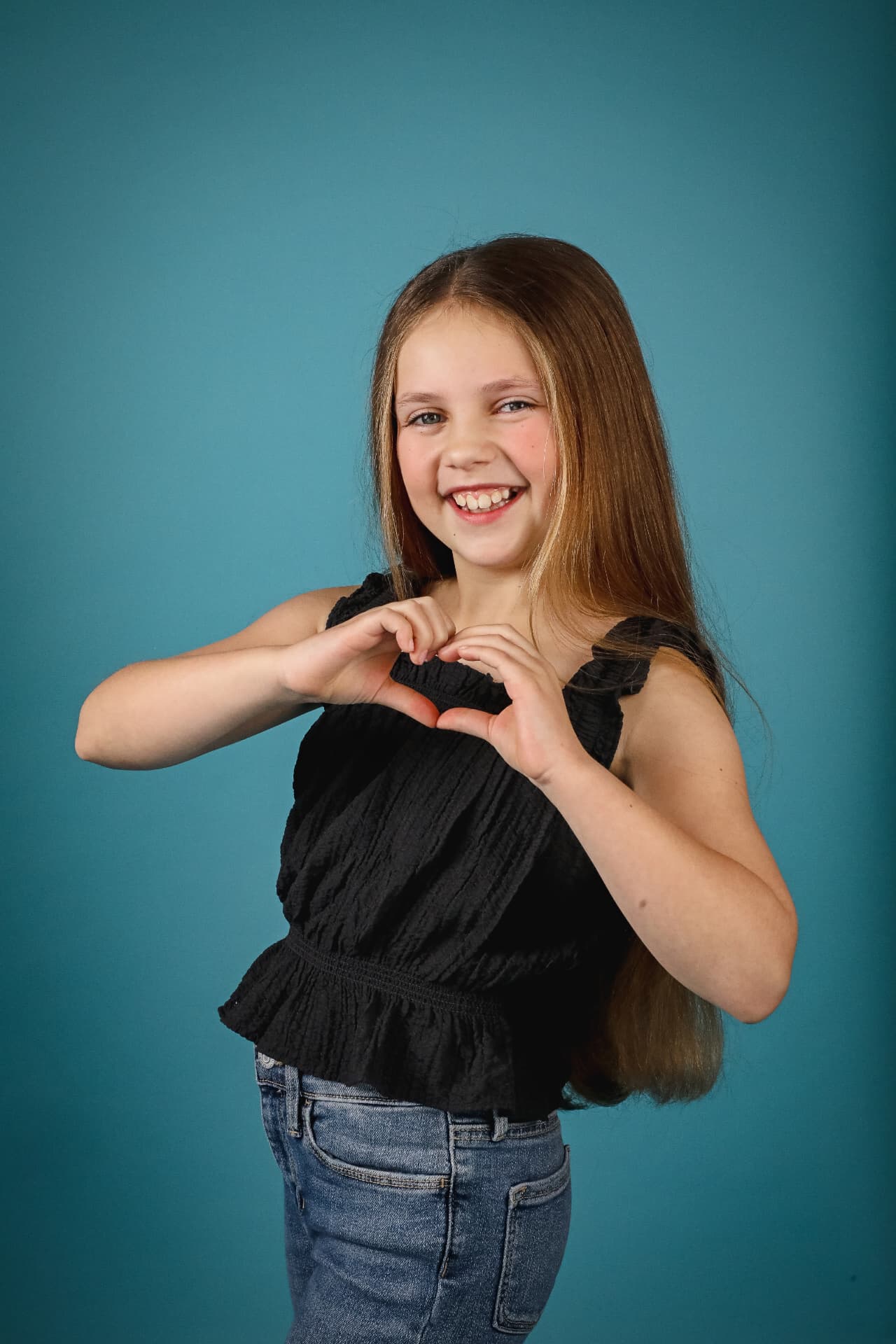 Olivia making a heart shape with her hands in front of a teal backdrop