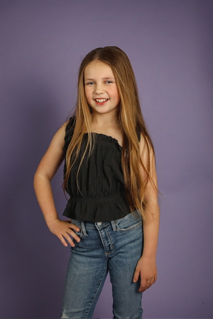 Full-length studio portrait of Olivia standing against a purple backdrop