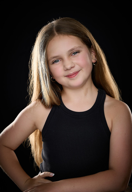 Olivia smiling with hands on her hips in a studio portrait on a black backdrop
