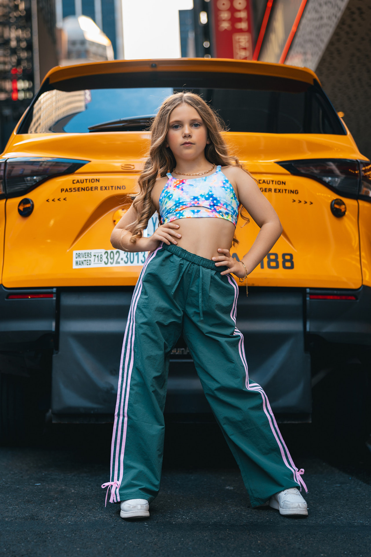 Olivia in a confident wide stance in front of the back of a yellow NYC taxi